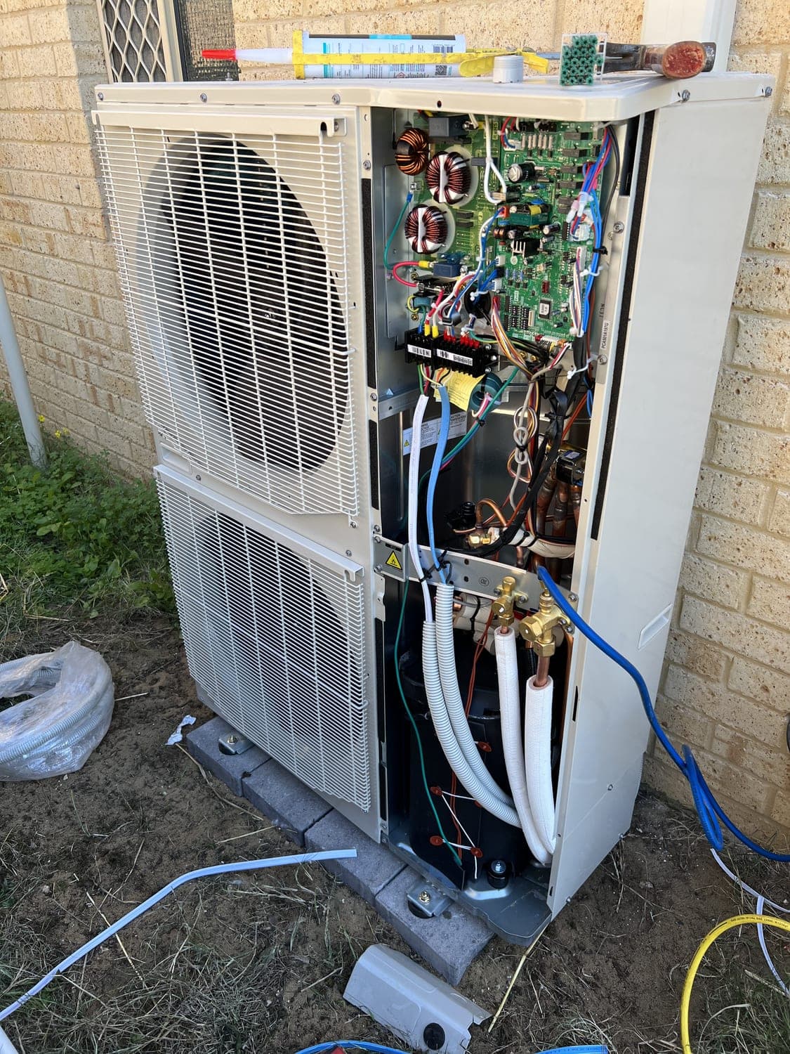 A split-system outdoor unit being serviced with the cover removed, exposing the coil and controls.