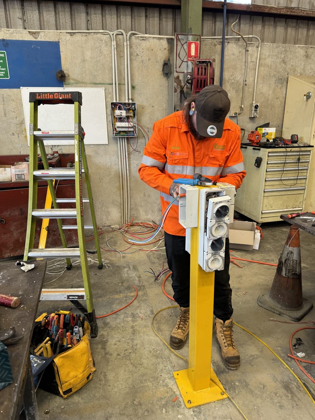 A Brady electrician in hi-vis wiring a pillar-mounted meter box.
